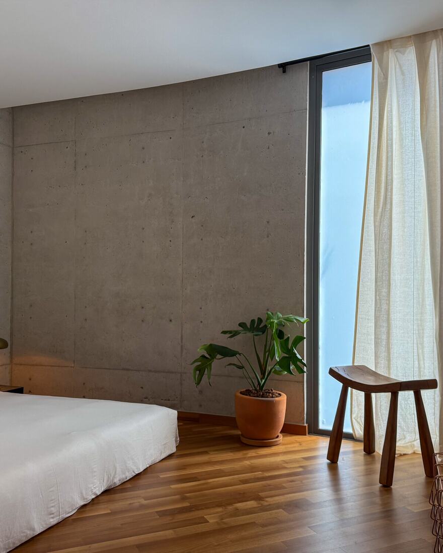 A brutalist apartment interior in Condesa with a bouclé sofa, textile wall hanging and a leafy terrace view.