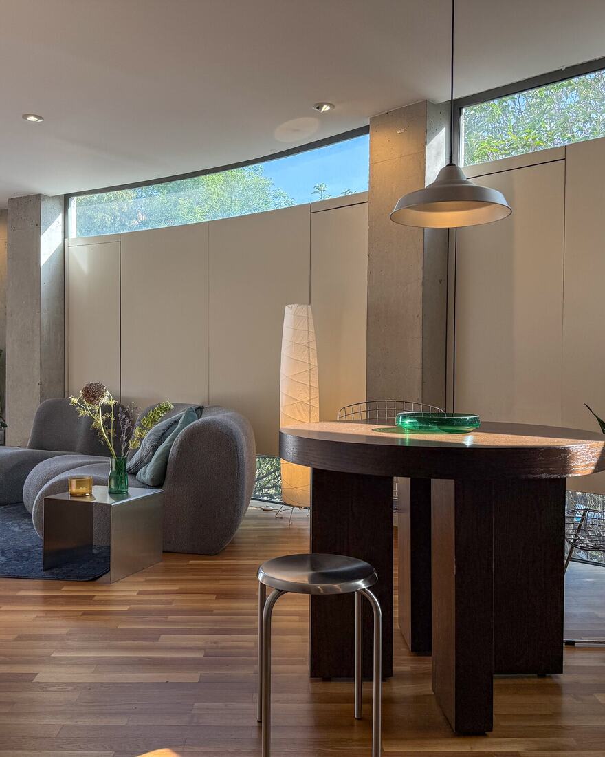 A brutalist duplex living area with sculptural seating, a paper floor lamp and a curved concrete wall.