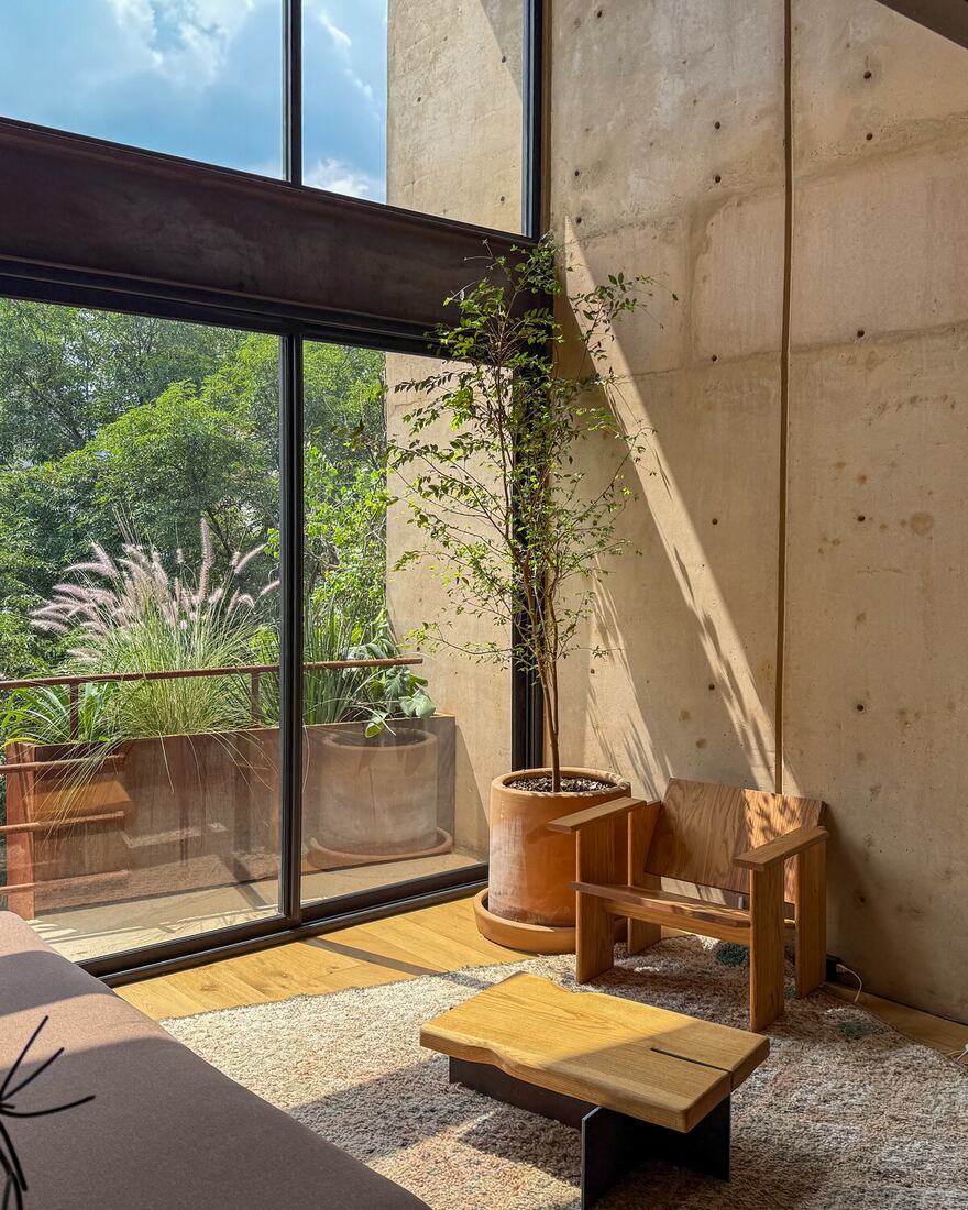 A double-height studio with a low bed, wooden furniture and full-height windows onto greenery.